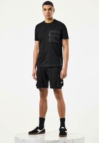 Sort t-shirt med lynlåslomme, parret med sorte cargo shorts. Funktioner inkluderer en afslappet pasform og matchende sneakers med teksturerede detaljer.