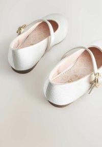 Balerini din satin alb cu bretele încrucișate, vârf rotund, cataramă aurie și o branț moale de culoare roz cu un model floral.