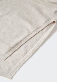 Tissu en maille beige clair avec un bord fini et une subtile fente latérale sur un fond uni.