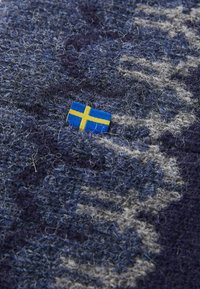 Small Swedish flag tag on textured dark blue and gray wool fabric with visible fibers and loops.