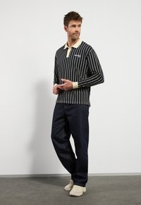 Zwart-wit gestreepte lange mouwen polo met een lichtgekleurde kraag, gecombineerd met donkere spijkerbroeken en beige sneakers.