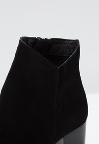 Stivaletto alla caviglia in camoscio nero con tacco alto a blocco e cerniera interna visibile, mostrato su uno sfondo chiaro uniforme.