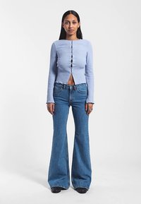 Ljusblå ribbad långärmad topp med knappar fram och mellanriktskärning, kombinerad med utsvängda blå denimjeans. Slät textur, figurnära design.