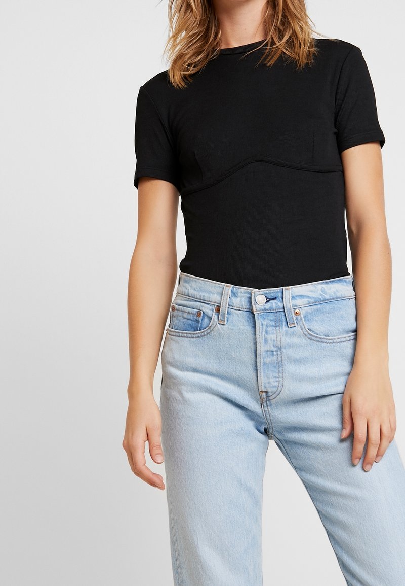 Top negro de manga corta ajustado con detalle de costura curva, combinado con jeans de tiro alto azul claro. Tela suave, corte casual.