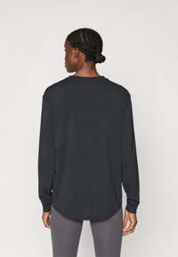 Μαύρο μακρυμάνικο μπλουζάκι με στρογγυλή λαιμόκοψη, φτιαγμένο από απαλό ύφασμα, με ραφή κατά μήκος της πλάτης και καμπύλη γραμμή στο τελείωμα.