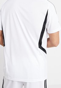 Vit träningsskjorta med korta ärmar; har svarta sidopaneler och en slät yta. Designad för aktiv användning med en avslappnad passform.