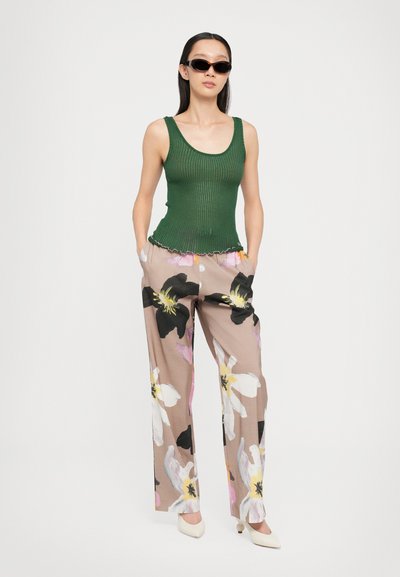 Grünes geripptes Tanktop mit gewelltem Saum, kombiniert mit beigen weiten Hosen mit großen schwarzen und rosa Blumenmustern. Abgerundet wird der Look mit eleganten Sonnenbrillen.