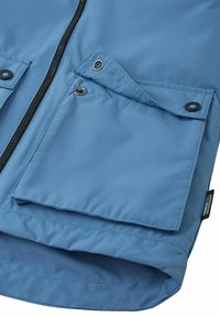 Giacca impermeabile azzurro chiaro con zip frontale, due tasche con patta e un'etichetta con la dicitura "Kinitotec Waterproof." Texture liscia.
