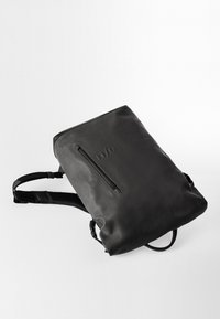Zaino nero realizzato in materiale liscio, dotato di una tasca con cerniera e spallacci regolabili. Design semplice con branding minimale.