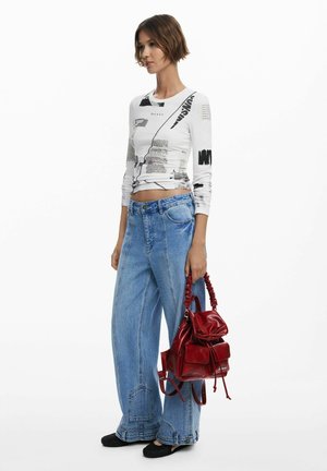 Weißes Langarmhemd mit schwarzen grafischen Drucken, kombiniert mit hochgeschnittenen, hellblauen weit geschnittenen Jeans und einem roten Leder-Rucksack. Schwarze flache Schuhe.
