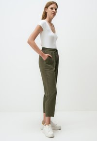 Body blanc côtelé associé à un pantalon vert olive à cordon de serrage avec poches latérales, jambes fuselées, et portant des baskets blanches.