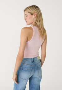 Ljusrosa ärmlös topp med en figurnära design, kombinerad med högmidjade blå denimjeans som har fem fickor och en etikett vid midjan.