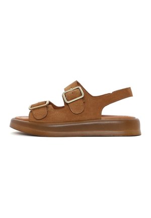 Sandalia de ante marrón con suela gruesa, dos hebillas ajustables sobre el pie y una tira abierta en el talón.