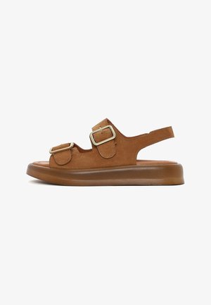 Sandale en daim marron avec semelle épaisse, deux brides ajustables à boucle sur le dessus du pied et une bride ouverte au talon.