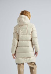 Long manteau en duvet beige avec capuche, design matelassé, poignets élastiques et ourlet à cordon de serrage. Matériau lisse et brillant avec une texture légèrement brillante.