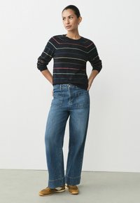 Marineblå sweater med flerfarvede striber, parret med løse blå denim jeans. Lysebrune sko fuldender outfittet. Enkel, afslappet stil.