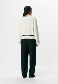 Maglione bianco a coste con rifiniture nere all'orlo e ai polsini, abbinato a pantaloni neri a gamba larga. Texture liscia, vestibilità morbida e stile casual.