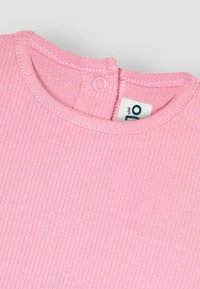 Rosa ribbad bomullstopp med rund halsringning och knappstängning bak. Har mjuk textur och en etikett med blå bokstäver.