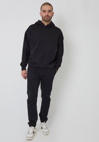 Černá mikina s volným střihem a přední kapsou typu kangaroo, spárovaná s tmavými kalhotami a bílými teniskami s černými akcenty.