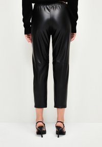 Zwarte faux leren broek met een elastische tailleband, cropped ontwerp en een soepele textuur, gecombineerd met zwarte hoge hakken.