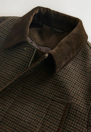 Brun rutig jacka med en kordflöjelkrage, med hel dragkedja och en sidoficka, tillverkad av mjukt, strukturerat tyg.