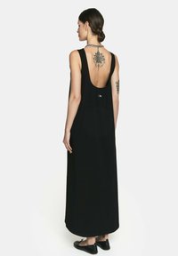 Czarna, bezrękawna sukienka maxi z otwartym plecami, z subtelnym akcentem logo i lekko zakrzywionym dołem. Gładki, lekki materiał.