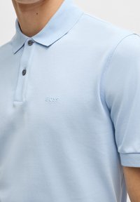 Polo bleu clair en tissu texturé, avec une patte de boutonnage à deux boutons et un logo brodé "BOSS" sur la poitrine.