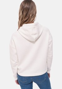Cremfarbener Hoodie mit Kordelzugkapuze, lässiger Passform und gerippten Bündchen. Kombiniert mit blauen Jeans.
