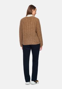 Brauner Strickpullover mit strukturierter Oberfläche, kombiniert mit dunkelblauen Hosen und weißen Sneakers, von hinten betrachtet.