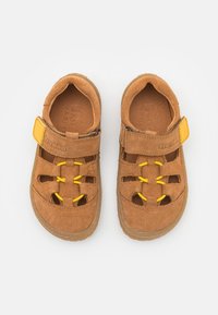 Brune semskede sandaler med gule detaljer, lukket tå-design, justerbar rem og perforerte åpninger for pusteevne. Gummisåle.