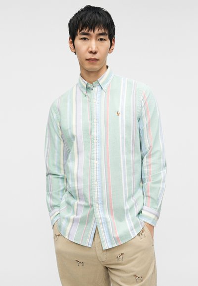 Φωτεινό πράσινο πουκάμισο με μακριά μανίκια και κουμπιά, με κάθετες πολύχρωμες ρίγες. Διαθέτει ένα μικρό κεντημένο λογότυπο στο στήθος.
