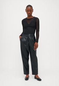 Haut noir transparent à manches longues avec un col en V et des détails en perles, associé à un pantalon en simili cuir noir taille haute et des ballerines noires.