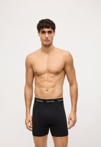 Boxer briefs negros de Calvin Klein con una cinturilla con logo, diseño ajustado y material de algodón suave, sobre un modelo con torso desnudo.