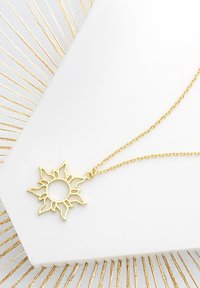 Guld solvedhæng med en delikat kæde, der har et åbent sol-design med strålende stråler, præsenteret på en hvid overflade.