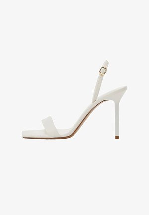 Sandale blanche à talon haut avec une fine bride à la cheville et une boucle dorée, bout ouvert, talon aiguille fin, vue de profil.
