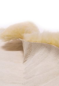 Helle beiges, strukturiertes Material mit einem weichen, flauschigen gelben Akzent. Das Design zeigt eine geschwungene Faltung, die seine natürliche Form betont.