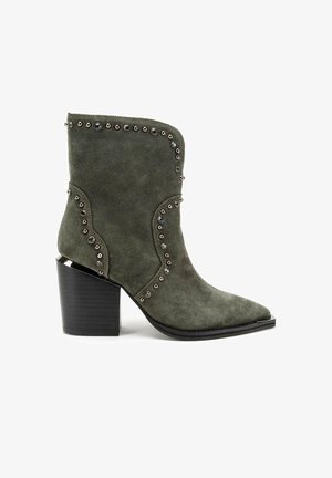Green suede ankle boot with pointed toe, metallic stud detailing along the seam, and a chunky black heel. Textured surface with smooth accents.