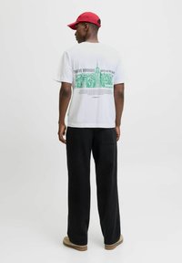 White t-shirt featuring green NYC skyline graphic on the back, paired with black wide-leg pants and a red cap. Simple, casual design.