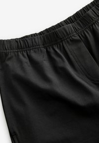 Černé šortky s elastickým pasem vyrobené z lehké, hladké tkaniny. Mají jednoduchý design s viditelným švem a bez vnějších kapes.
