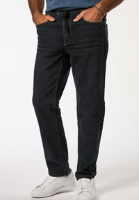Pantalones jogger de denim oscuro con cintura elástica y cordón. Bolsillos laterales y líneas de textura sutil; combinados con zapatillas blancas.