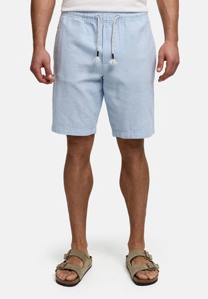 Mand iført lyseblå shorts med snøre og beige sandaler med dobbelt rem, stående mod en hvid baggrund.