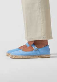 Scarpe espadrillas blue suede con punta rotonda, cinturino alla caviglia e suola in juta intrecciata. Abbinato a pantaloni cropped beige chiaro.