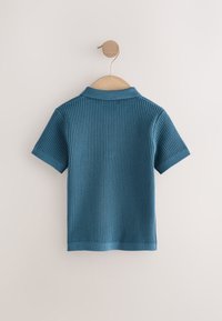 Blauw geribd kort mouw gebreid shirt met kraag, hangend aan een houten kledinghanger tegen een effen lichte muur.