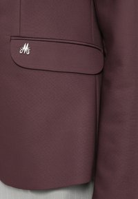 Blazer bordeaux con una superficie liscia, dotato di una tasca sul petto e un accento in logo argento sulla tasca.