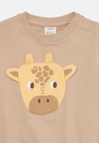 Beige sweatshirt med en texturerad gul giraffapplikation på framsidan, med svarta och bruna detaljer för ögon och fläckar. Tryckknappsstängning på axeln.