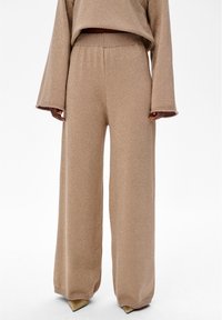 Beige wijde broek met een lichte glans, voorzien van een elastische tailleband en een medium-dikke gebreide textuur. Soepele, losse pasvorm over de hele lengte.