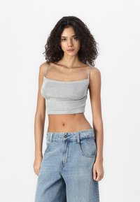 Hallhalli ribaga crop top õhukeste rihmadega, kombineeritud lõtvade helesiniste denim-pükstega. Riietusel on elastne tekstuur ja vormitud siluett.