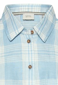 Light blue and white plaid button-up shirt collar with brown buttons and "camel active" label inside the neckline.