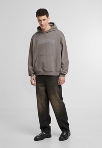 Grå hættetrøje med teksten "Trust Issues", forlommer og ribbede manchetter. Parret med mørke, slidte jeans og sorte chunky sko.