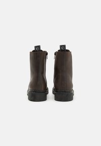 Botas de cuero marrón hasta el tobillo con un acabado suave, cremalleras laterales y suelas de goma negra. Incluyen tiradores en la parte posterior para facilitar su uso.